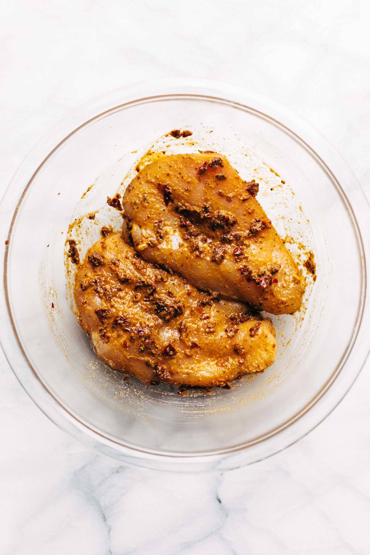 Raw chicken in a bowl with seasonings.