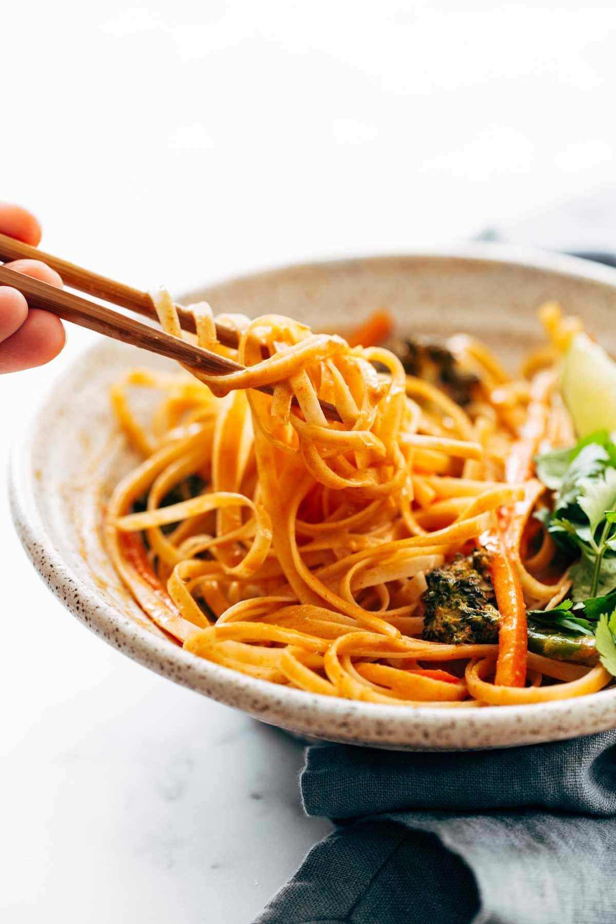 Taking a bite of red curry noodles with chopsticks.