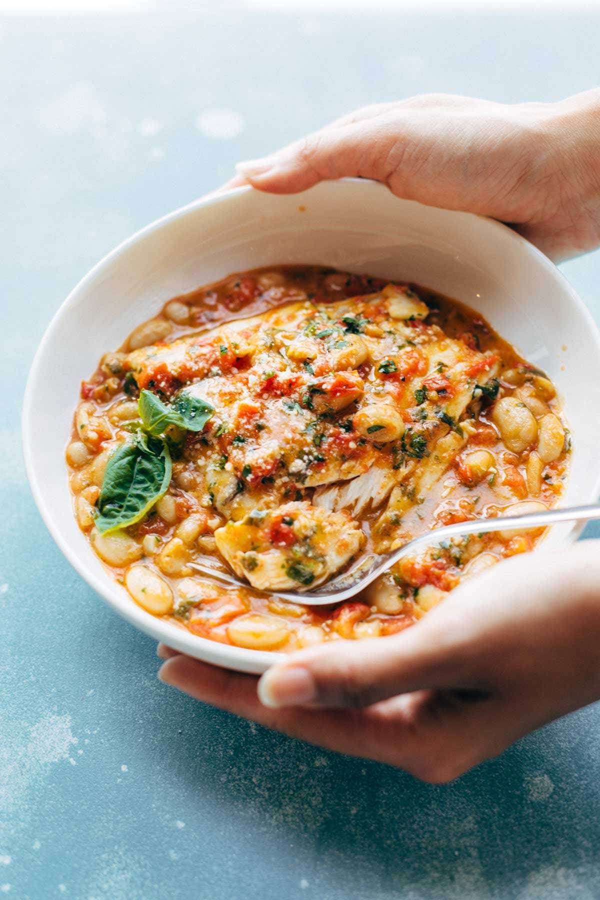 Hands Holding a bowl of Garlic Basil Barramundi Skillet with Tomato Butter Sauce.