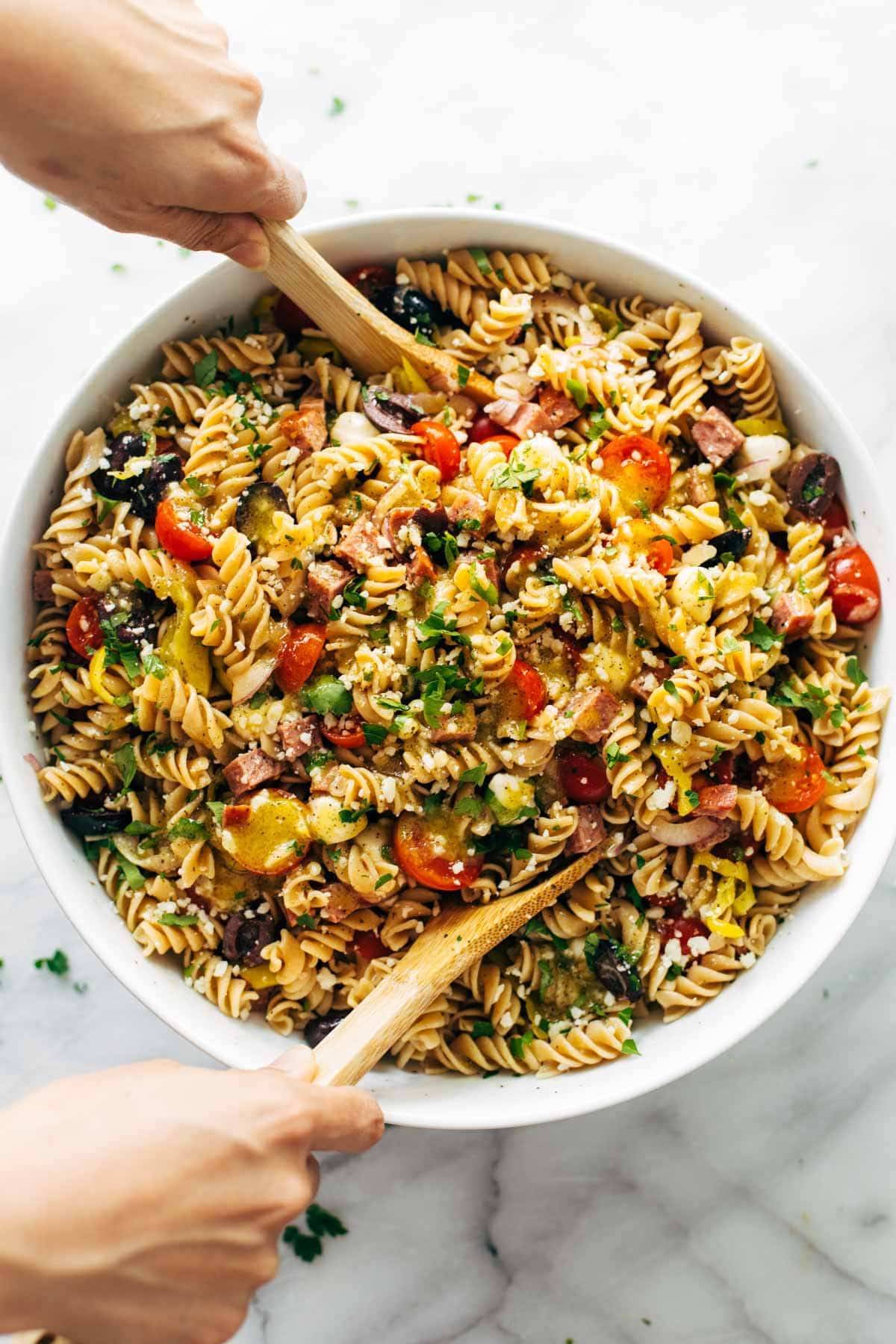 Pasta salad being mixed with spoons.