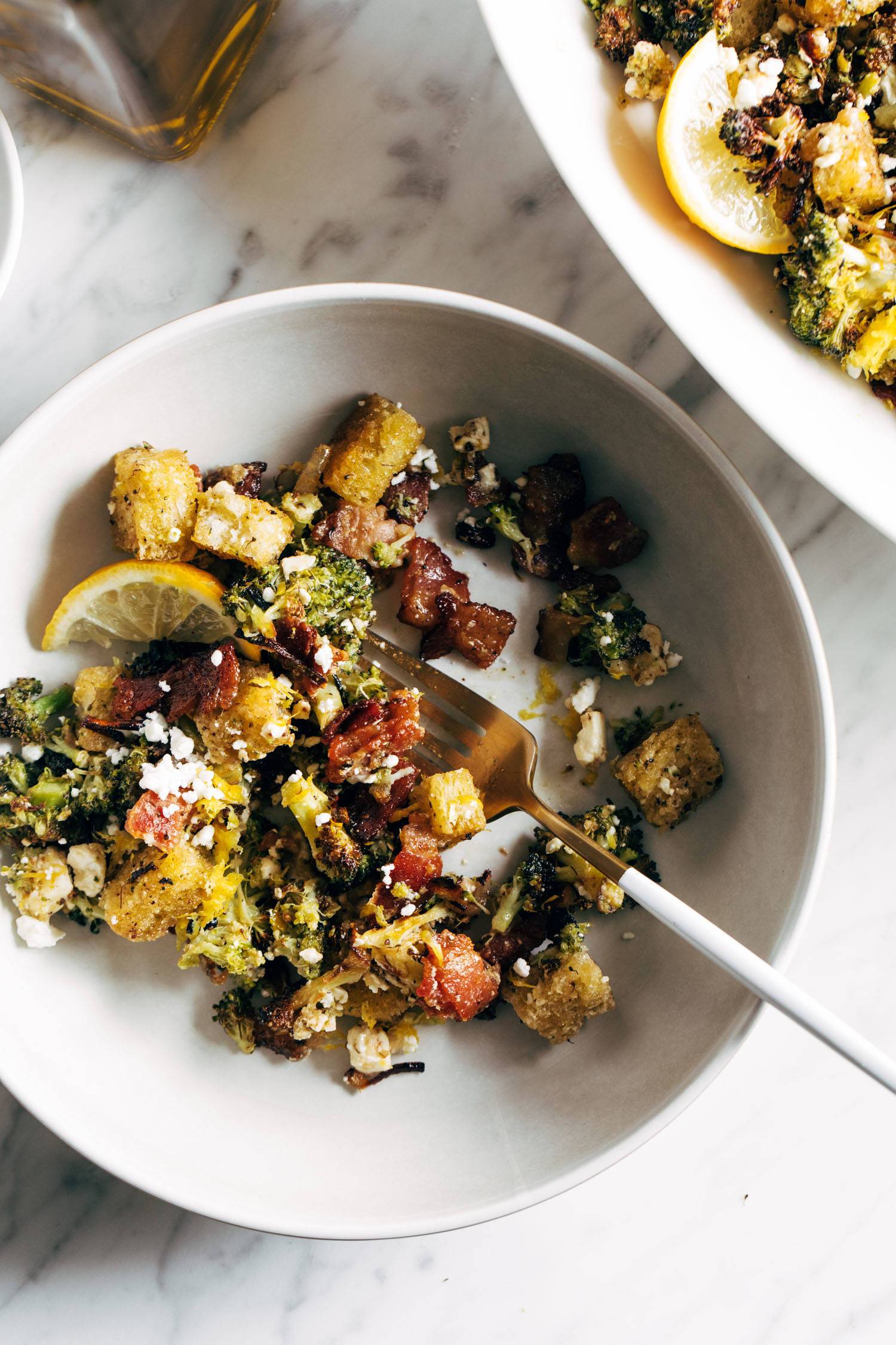 Roasted broccoli salad on a plate with lemon slices and a fork. 