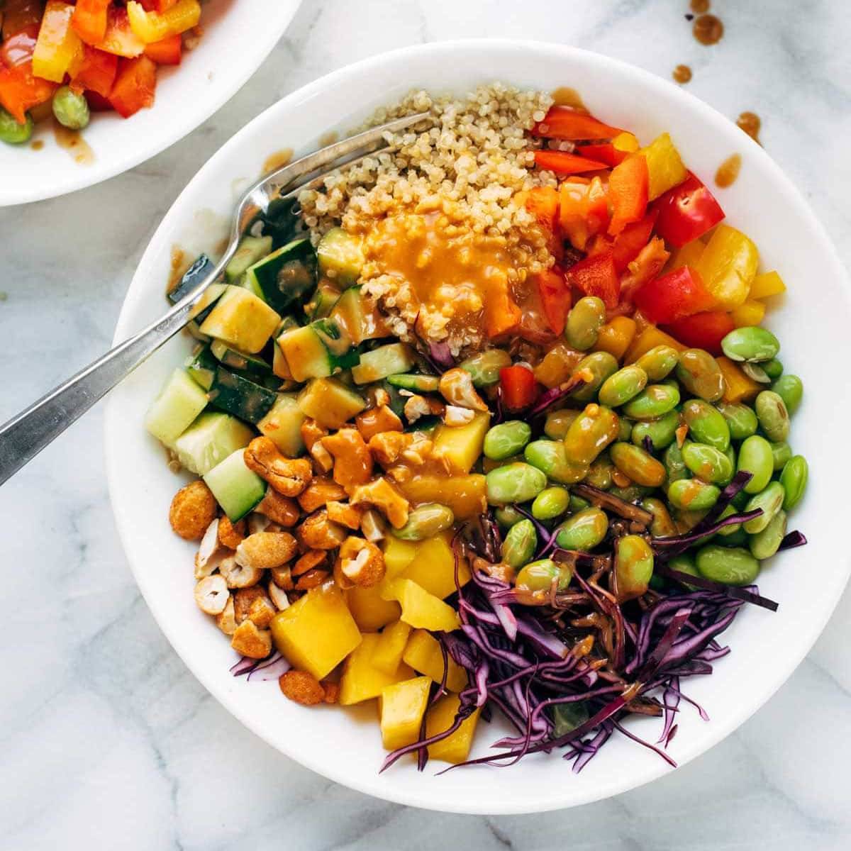 A colorful mix of veggies and quinoa in a bowl with peanut dressing and cashews. 