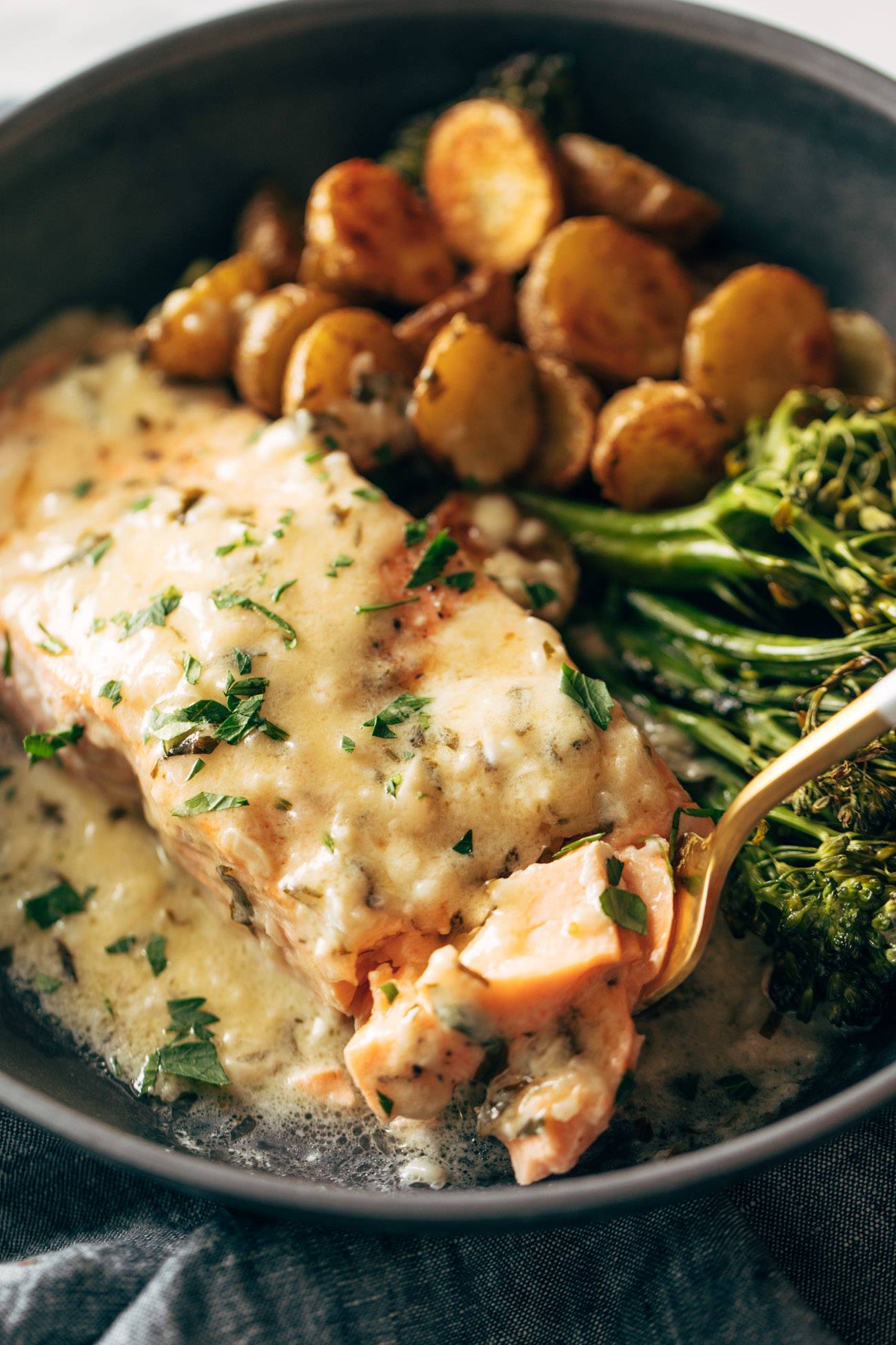 Close-up of fork taking a bite out of baked salmon in a bowl. 