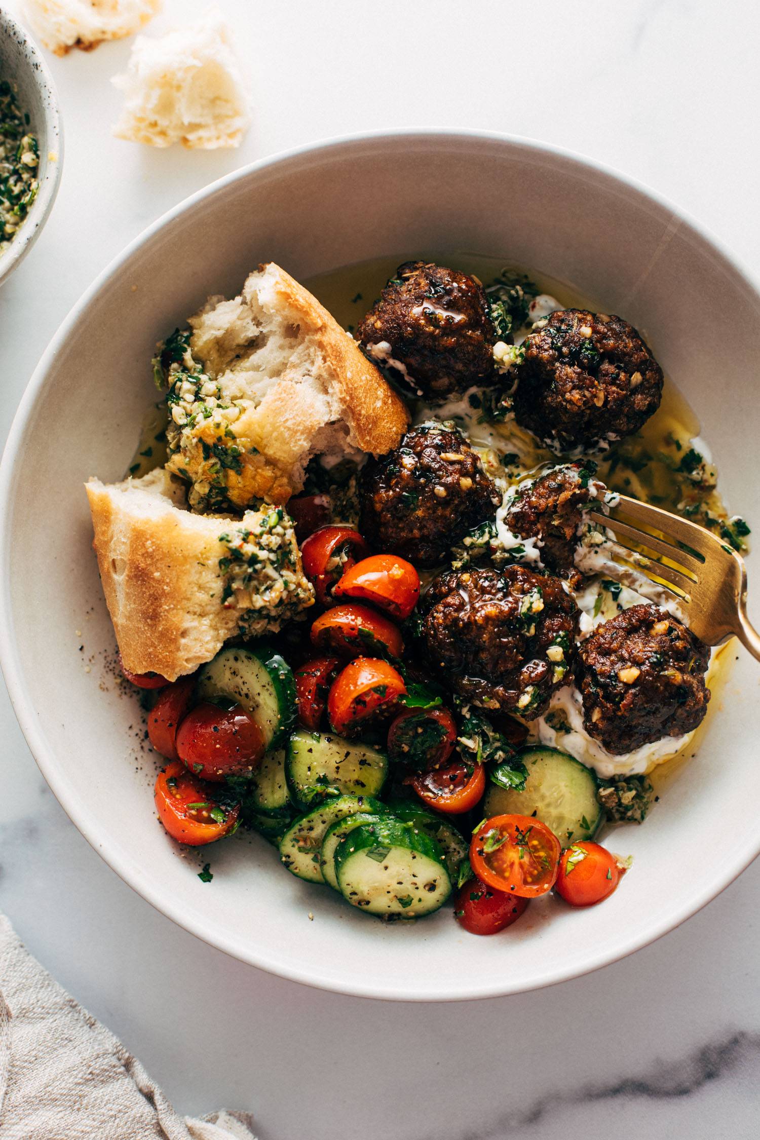 Meatballs in a bowl with a tomato salad, fork, and bread